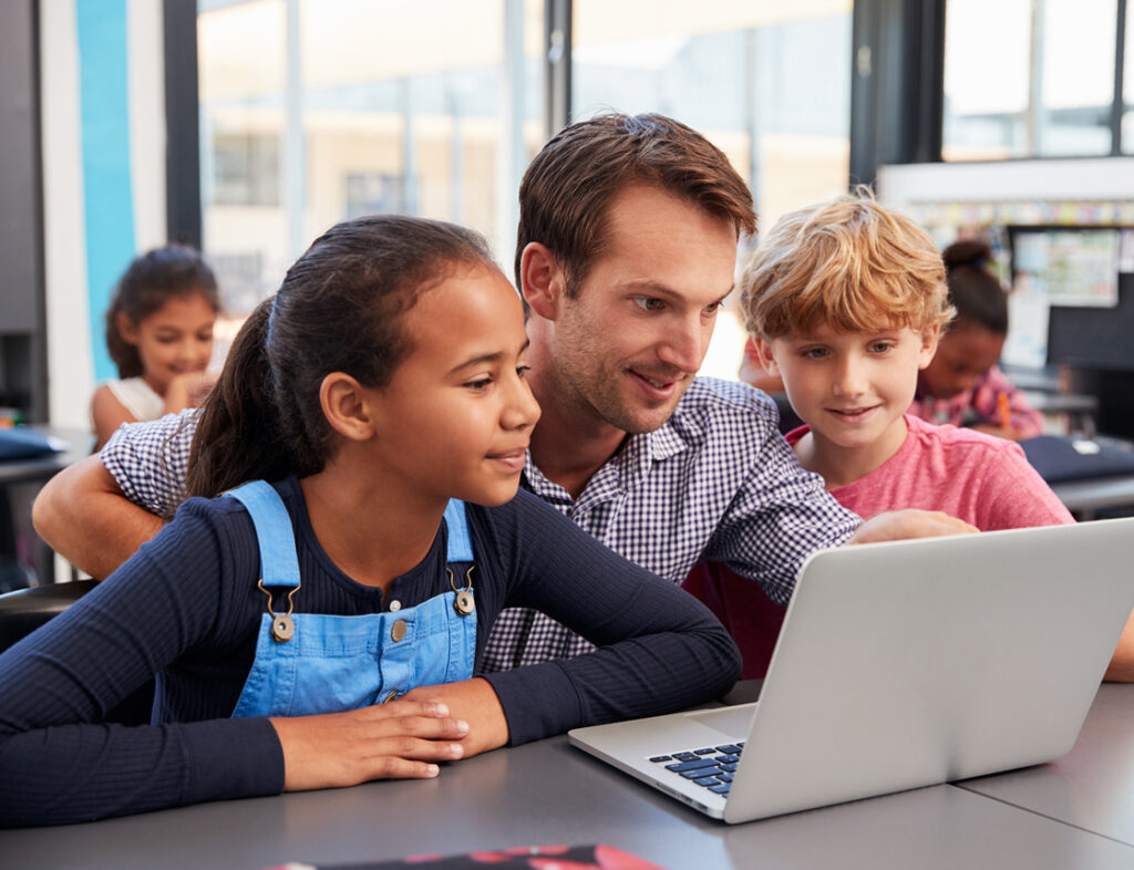 Photo showing a teacher helping two children to use a laptop