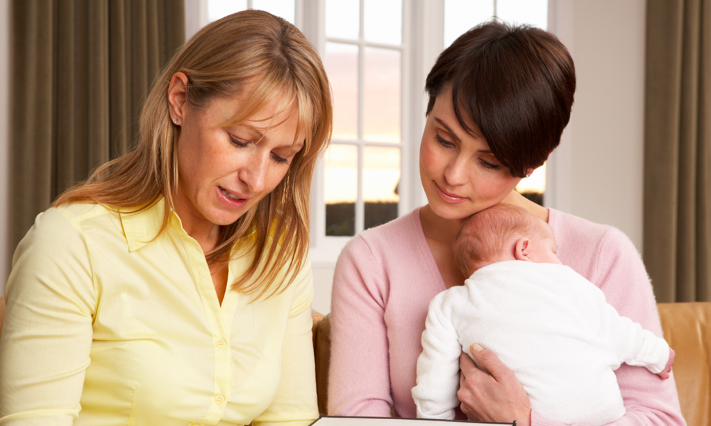 Photo showing two women looking at a form, the woman on the right is holding a baby