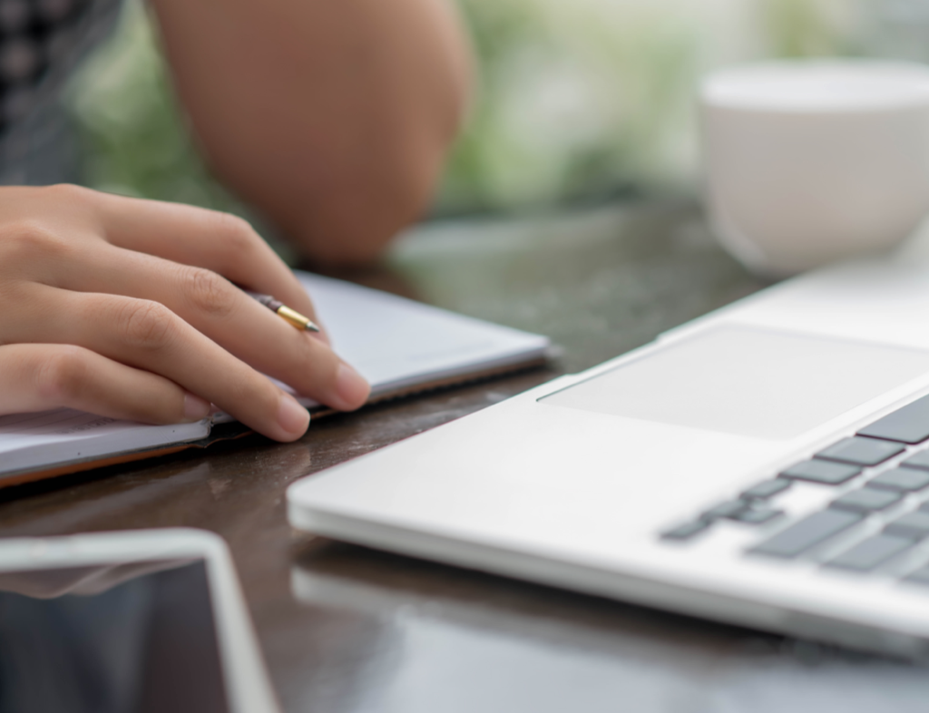 Photo showing a person with a pen and notepad looking at a laptop