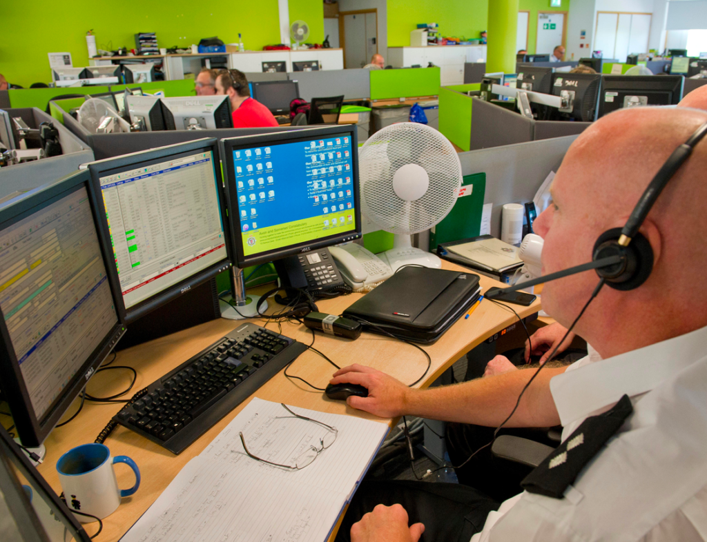 Photo showing a policeman working at a desk with three computer monitors