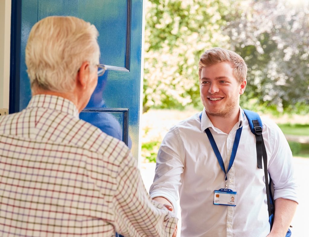 Photo showing a social worker shaking hands with an enderly man on his doorstep