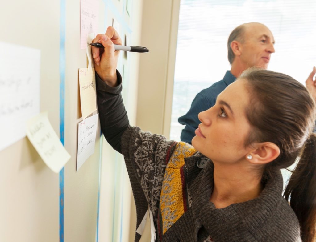 Photo showing a woman writing on a post it note on a wall