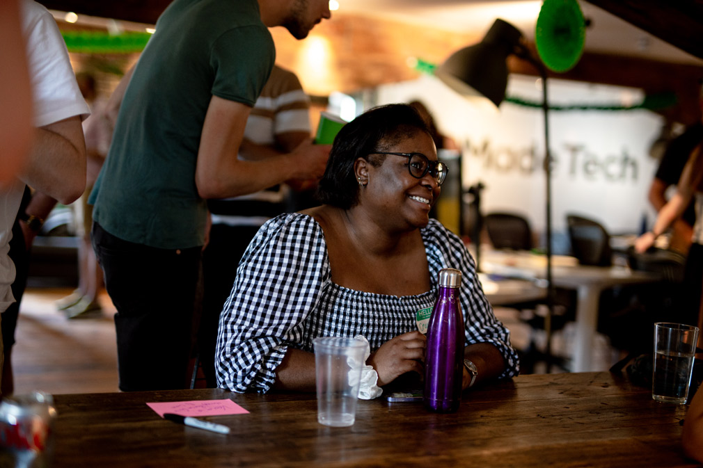 Photo of a woman sitting at a table surrounded by people and smiling with a waterbottle