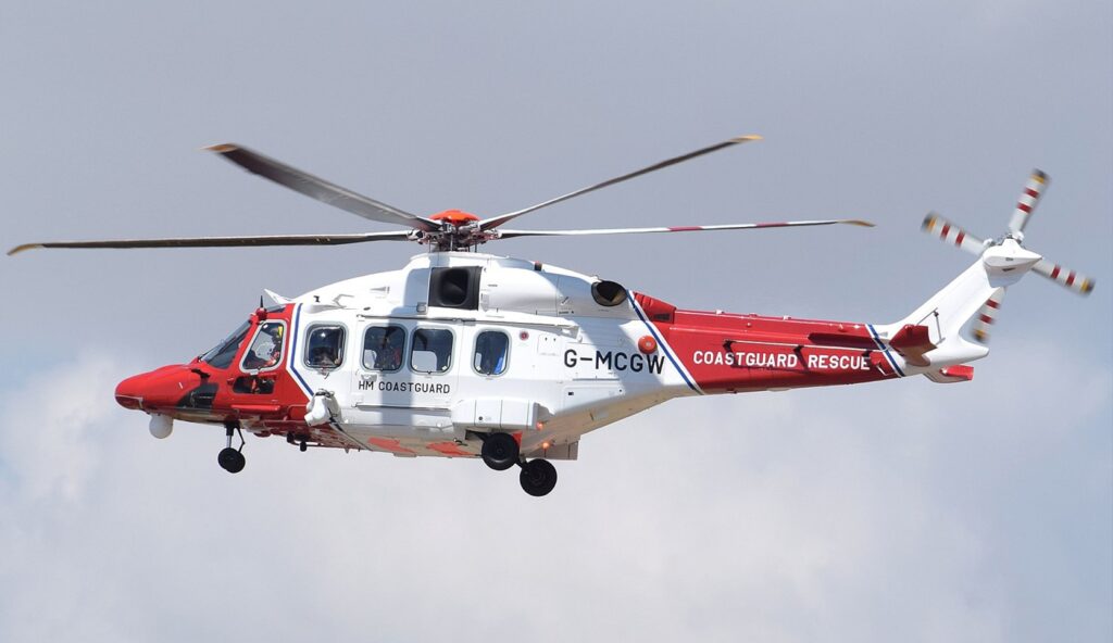 Image of a HM coastguard helicopter with red and white flying in a cloudy sky
