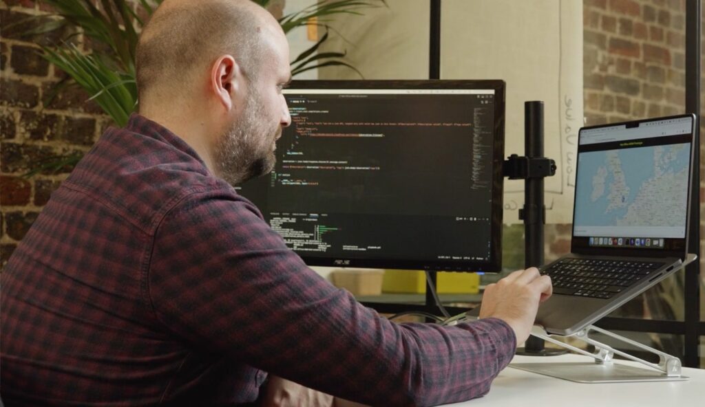 Man sitting at a desk in front of an open laptop with a map of the UK